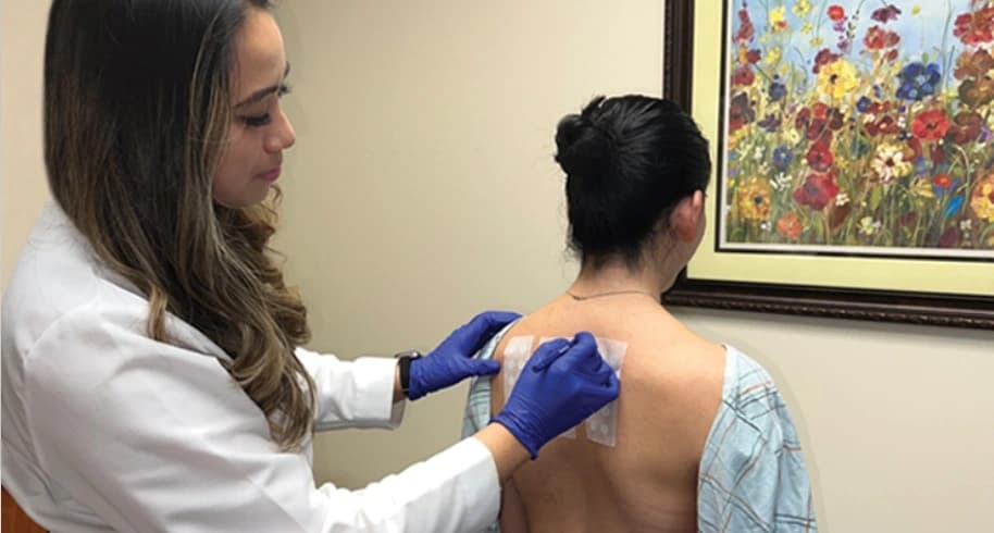 A clinician wearing gloves applying allergen patch strips to a patient's upper back during patch testing